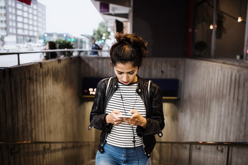 woman looking down at mobile phone walking out of tunnel