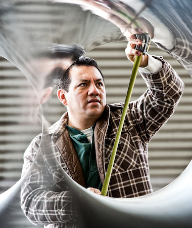 Hispanic man factory worker measuring diameter of pipe in a sheet metal factory.