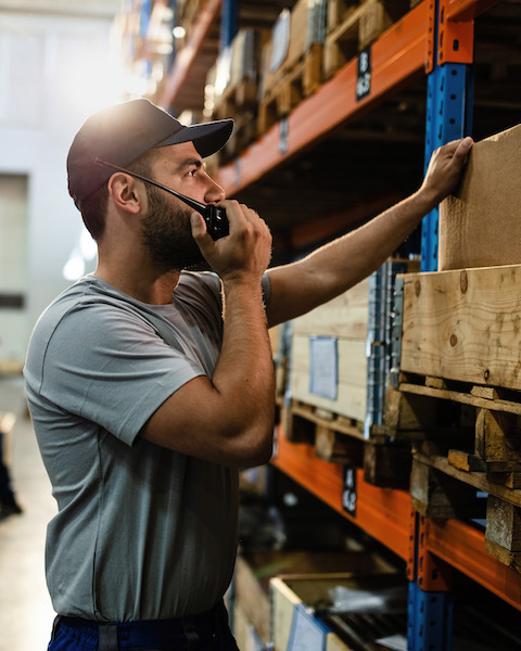Young man communicating over walkie-talkie while working in industrial storage compartment.