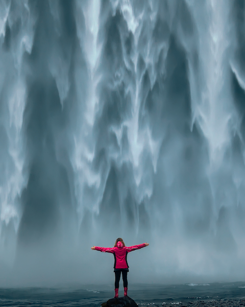 landscape photo of brave girl who proudly standing with his arms raised in front of water fall