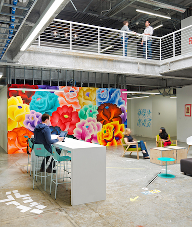Inside view of Meta office with employees seated around tables and bright painted mural wall